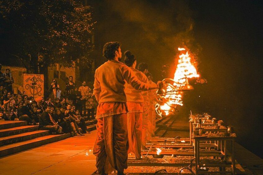 A nighttime outdoor event with a large fire, people sitting on steps, and a crowd watching. 3