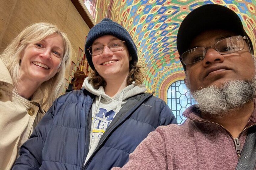 Three people in a room with a colorful, patterned ceiling and a stained glass window. 2