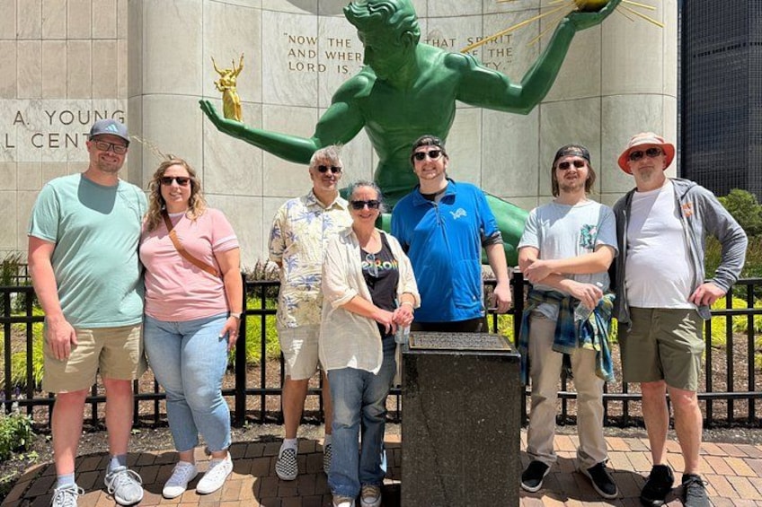 A group of people standing in front of a building with a large green statue and a plaque with text. 1