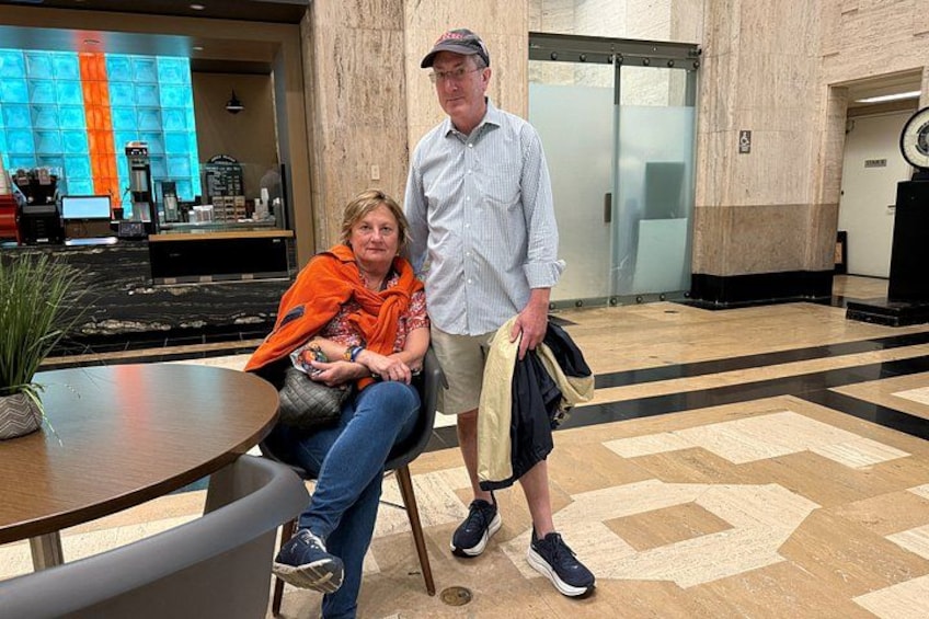 Two people sitting at a table in a lobby with a patterned floor and a coffee machine in the background. 5