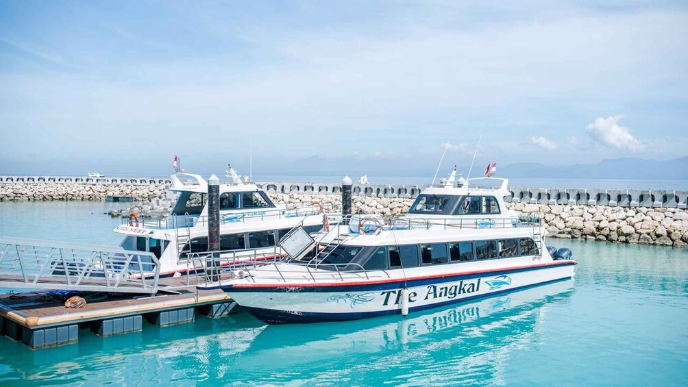 Two boats docked at a pier with a rocky breakwater in the background. 1