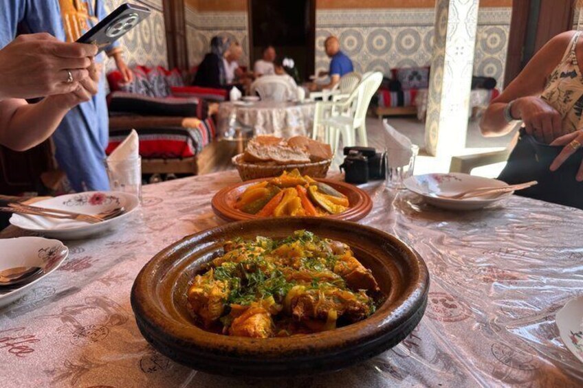 A dining table with a large clay pot of stew, a bowl of fries, and a plate of bread. 2
