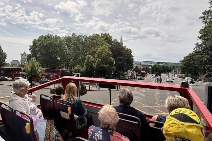 A red double-decker bus with passengers seated, a street with trees, and a building in the background. 5