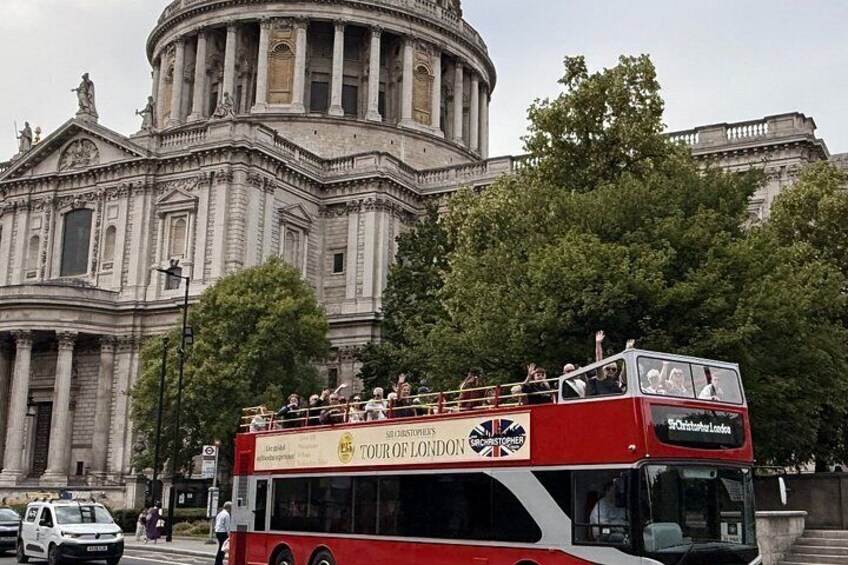A red double-decker bus with tourists on top, passing by a large classical building with columns. 3