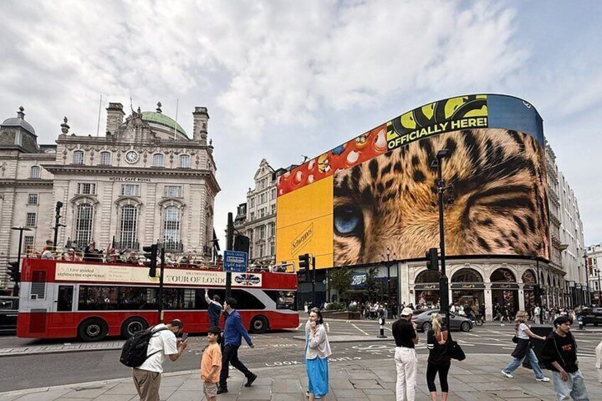 A busy street with a large billboard, a red double-decker bus, and historic buildings. 4