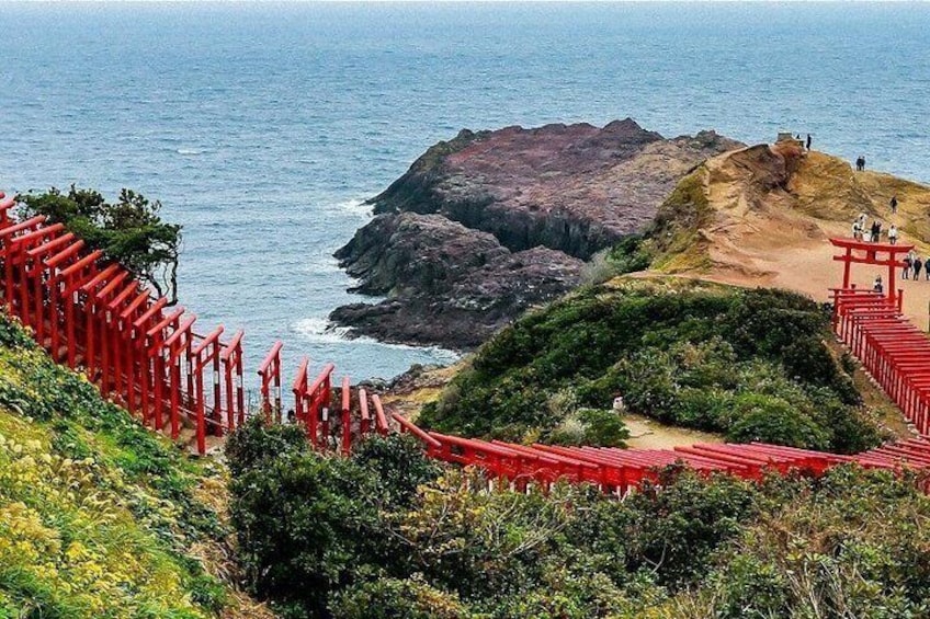 A coastal landscape with a red torii gate pathway leading to a rocky outcrop by the sea. 1