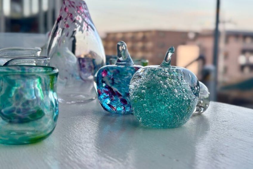 Three glass containers with a reflective surface, placed on a white surface with a blurred cityscape in the background. 2