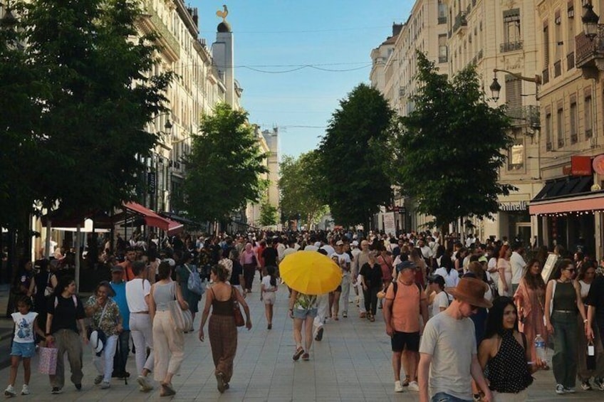 A busy urban street with pedestrians, trees, and historic buildings. 2