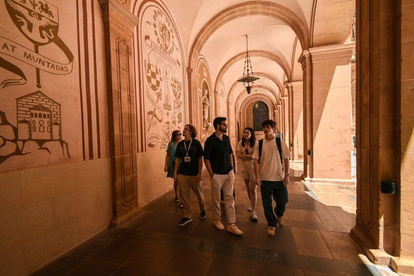 A group of people walking in a corridor with arches and wall decorations. 2