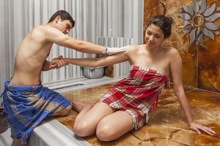 A man and a woman in a bathroom, with the man applying lotion to the woman's back. 2