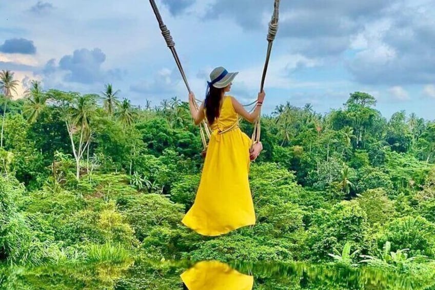 A person in a yellow dress swinging on a rope swing over a lush green landscape. 4