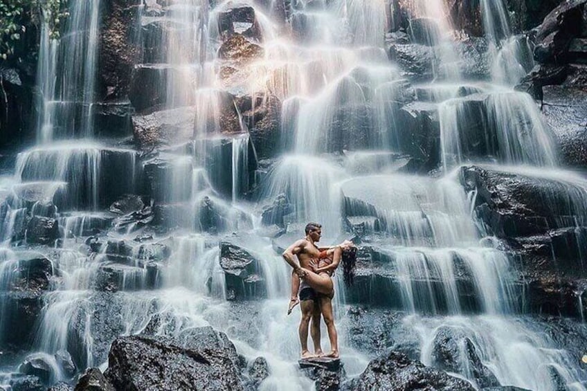 A waterfall with a person standing on rocks in the foreground. 2