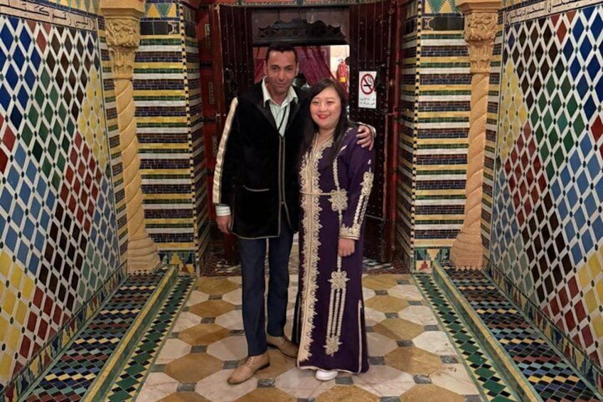 A hallway with patterned tile flooring and walls, a person in a dark vest and jeans, and another in a long, ornate dress. 4