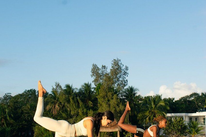 Two people performing a yoga pose outdoors with trees and a building in the background. 1