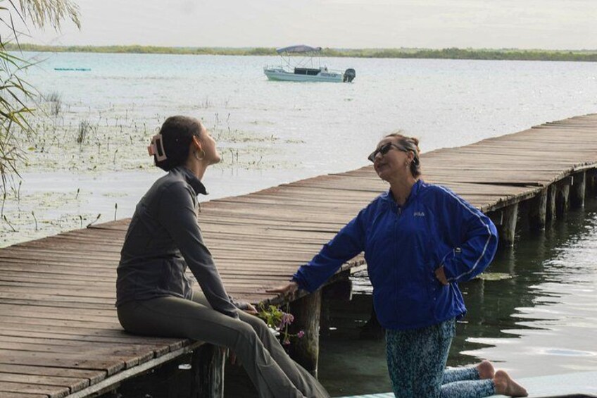 Two people on a wooden dock by a calm body of water with a boat in the distance. 2