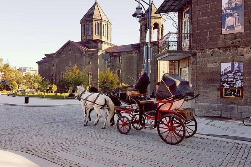 A horse-drawn carriage on a cobblestone street, a church with a bell tower, and a building with a balcony. 1