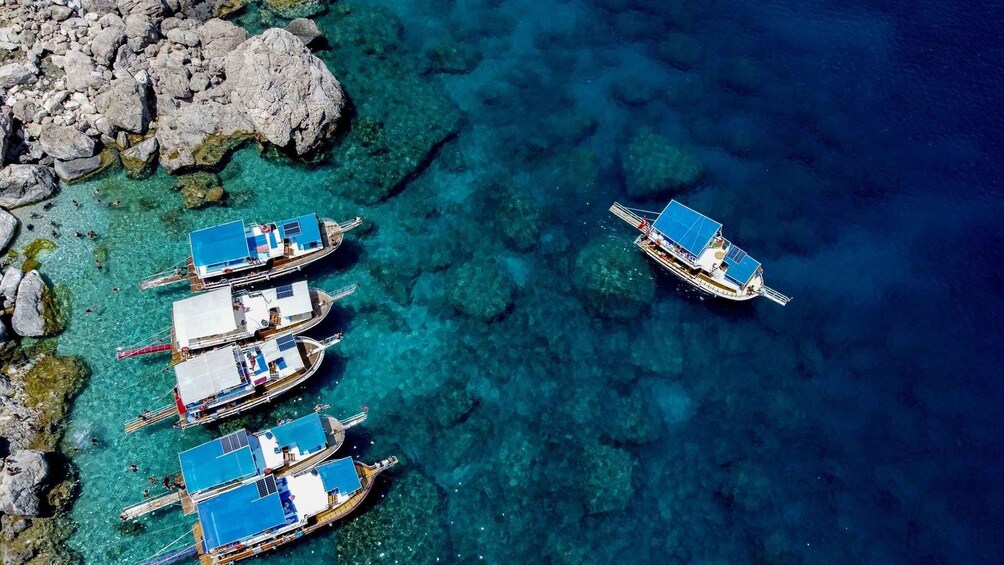 A group of boats anchored near a rocky shoreline in clear blue waters. 5