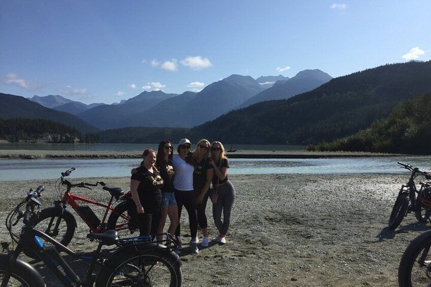 A group of people standing by a lake with mountains in the background. 2