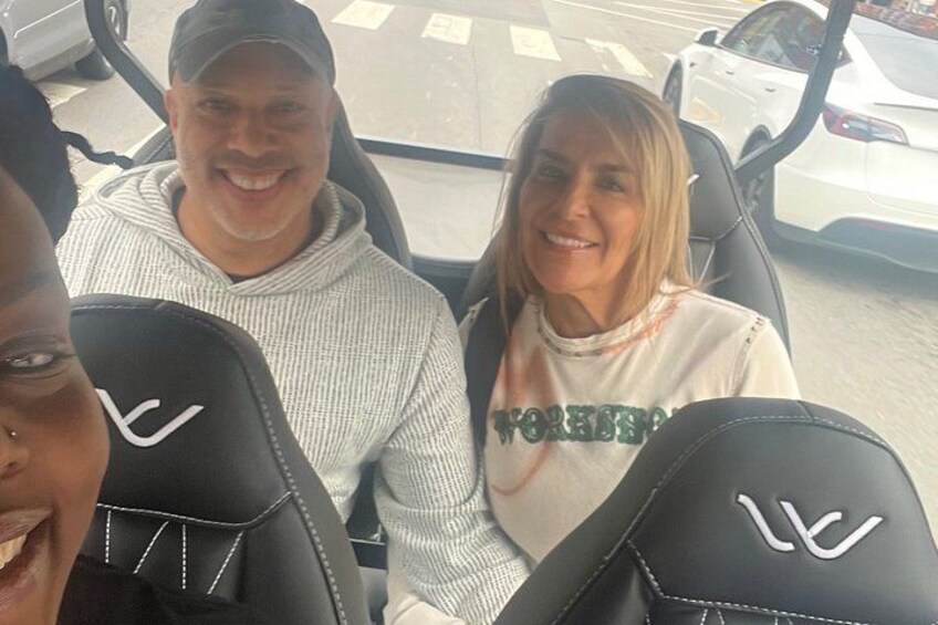 Three people in a vehicle with visible seat designs and a car in the background. 3