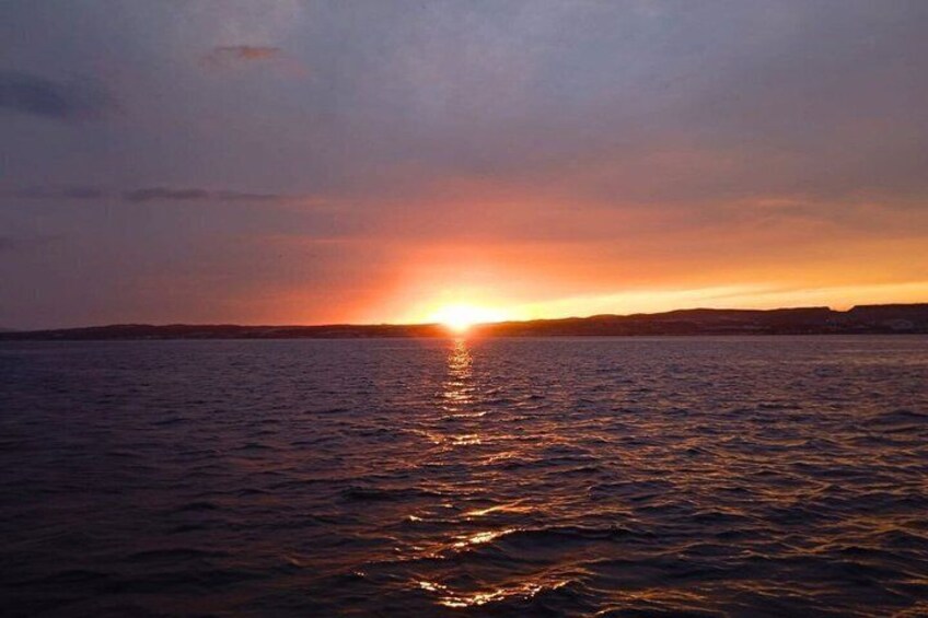A sunset over a calm sea with a distant shoreline. 1