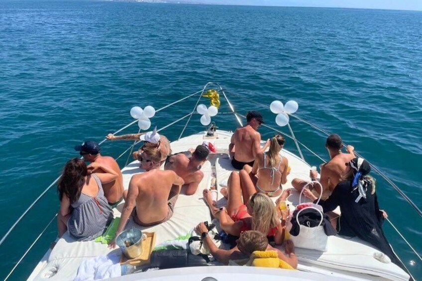 A group of people on a boat with white balloons and a clear blue sea. 2