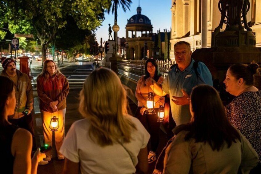 A group of people gathered around a street lamp in a city square at night. 1
