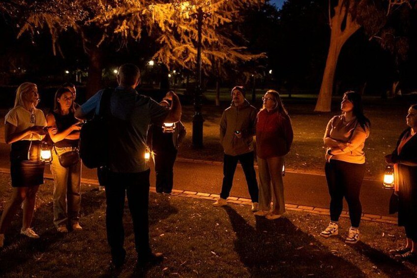 A group of people standing on a sidewalk at night, holding lanterns. 4