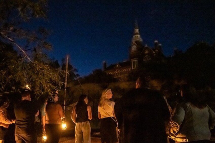 A group of people gathered outdoors at night, some holding lanterns, with a church steeple in the background. 4