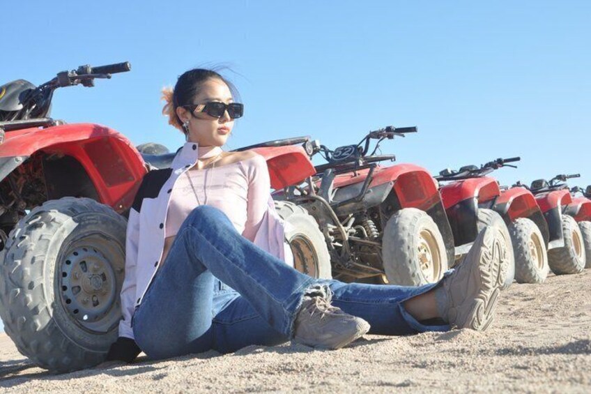 A person sitting on the ground with red quad bikes in the background. 4