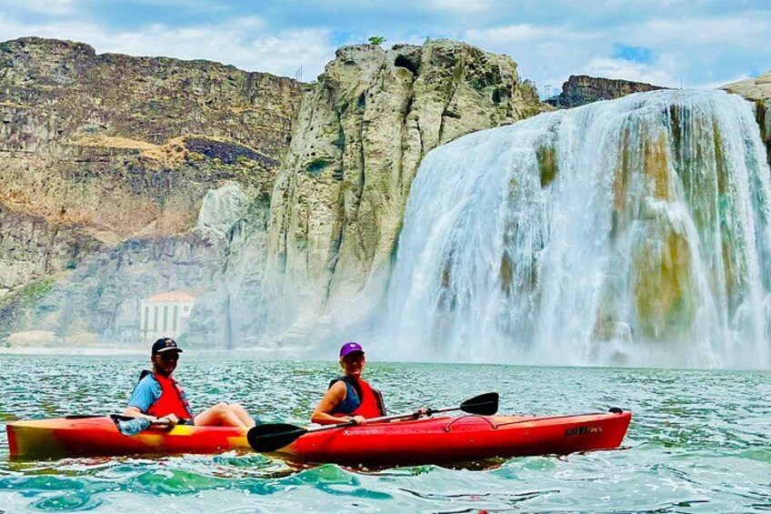 Two people kayaking on a calm body of water with a large waterfall in the background. 4
