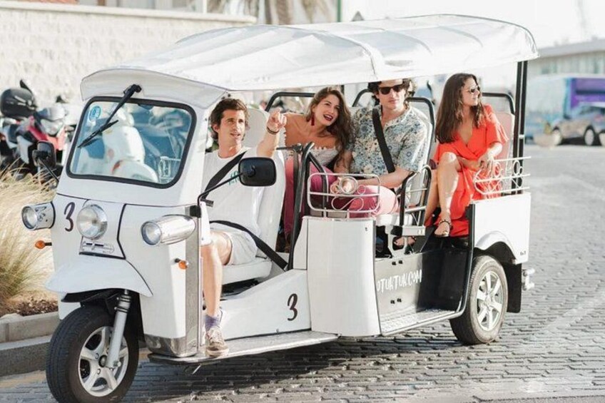 A white three-wheeled vehicle with passengers, number 3, on a cobblestone street. 5
