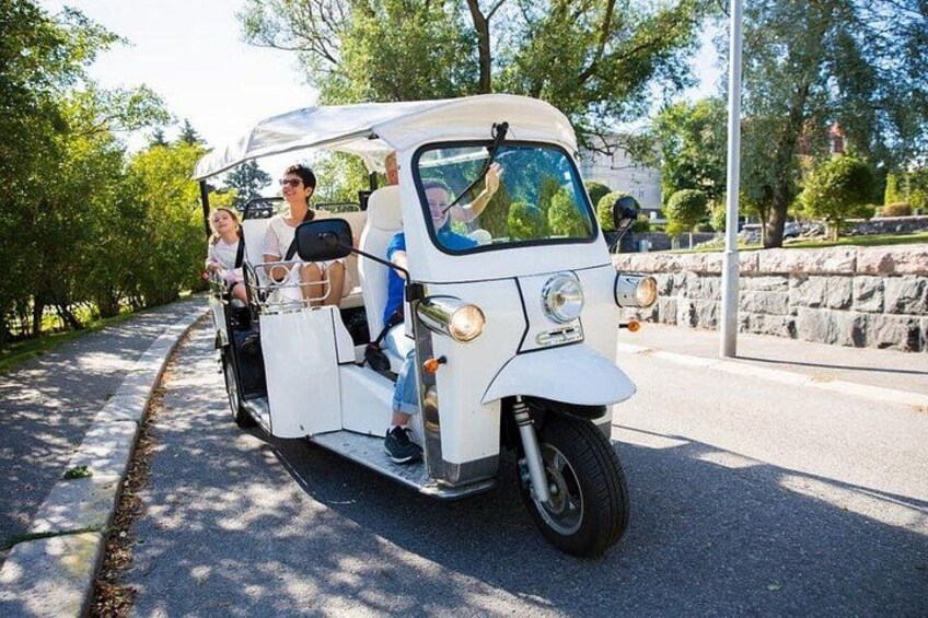 A white golf cart with passengers on a paved road surrounded by trees. 3