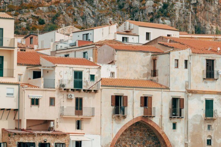 A coastal town with terracotta-roofed buildings, a prominent archway, and rocky cliffs in the background. 2