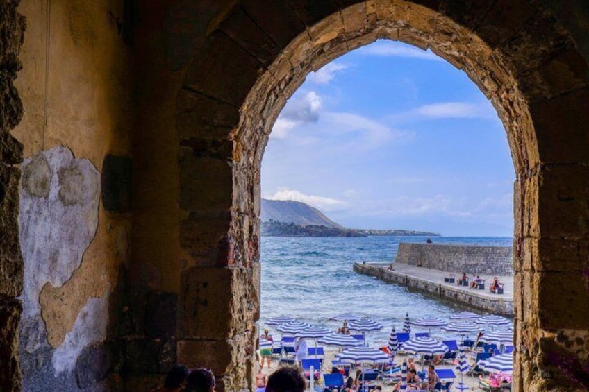 An arched stone structure overlooking a beach with striped umbrellas and people. 3