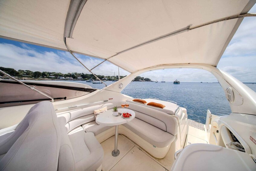 A boat's interior with a cushioned seating area, a small table with a drink, and a view of the water and distant boats. 5