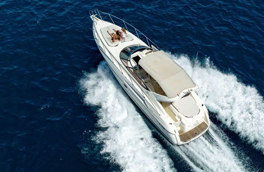 A white yacht with a covered stern, two people on deck, and wake behind it. 2