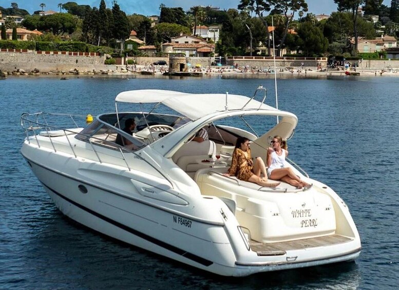 A white yacht named 'WHITE PEARL' on calm waters with a beach and houses in the background. 1