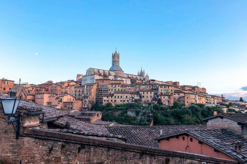 A historic cityscape with a prominent dome and bell tower, terracotta rooftops, and a clear sky. 4
