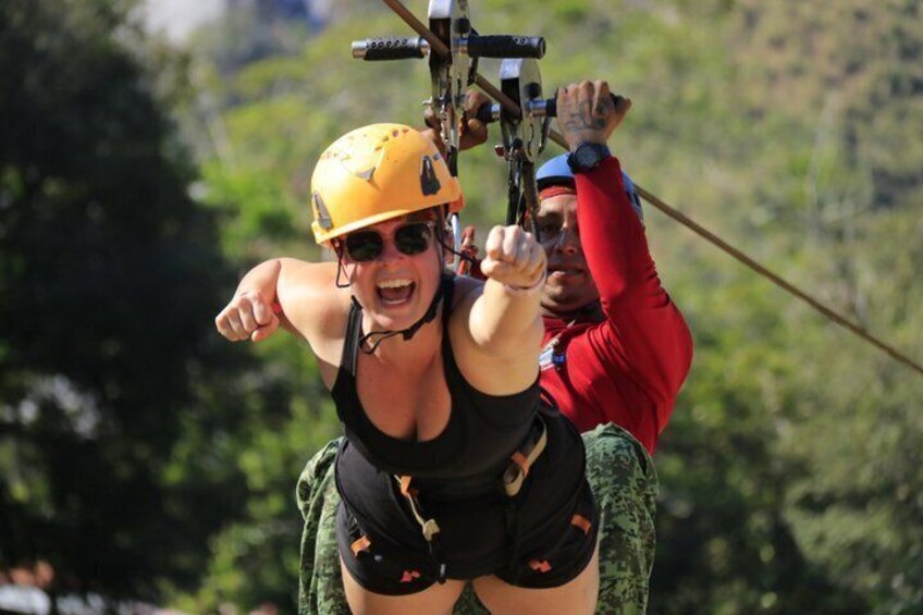 A person in a harness and helmet, being pulled by a rope, with a guide in a red shirt. 1