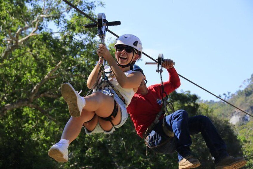 A person zip-lining with a harness and helmet, another person assisting, and a forested landscape in the background. 3