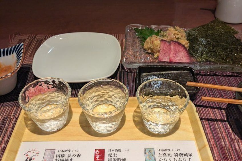 A Japanese meal with sashimi, a white plate, and three glasses of sake. 1