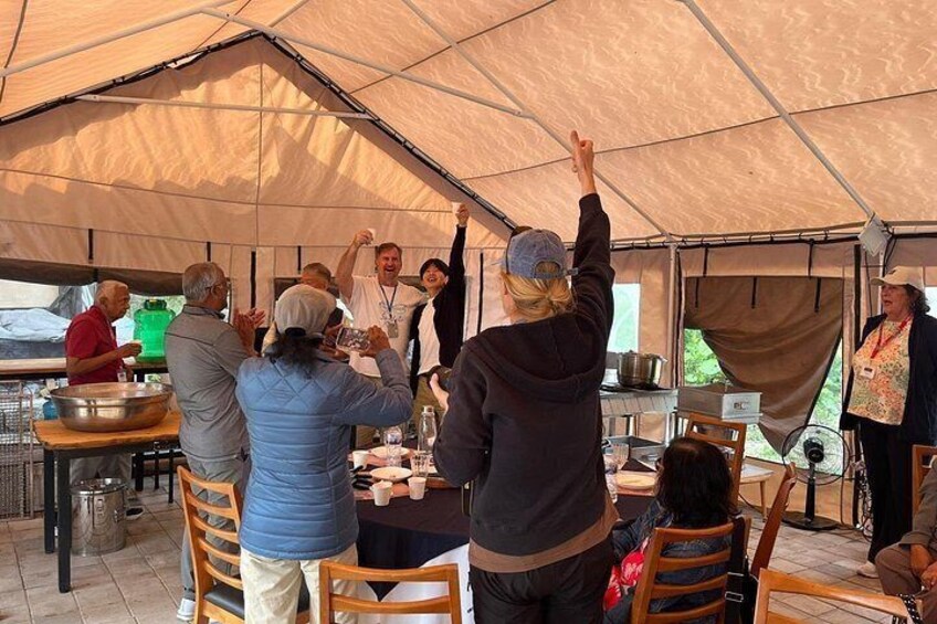 People gathered around a table under a tent, some raising their hands. 4