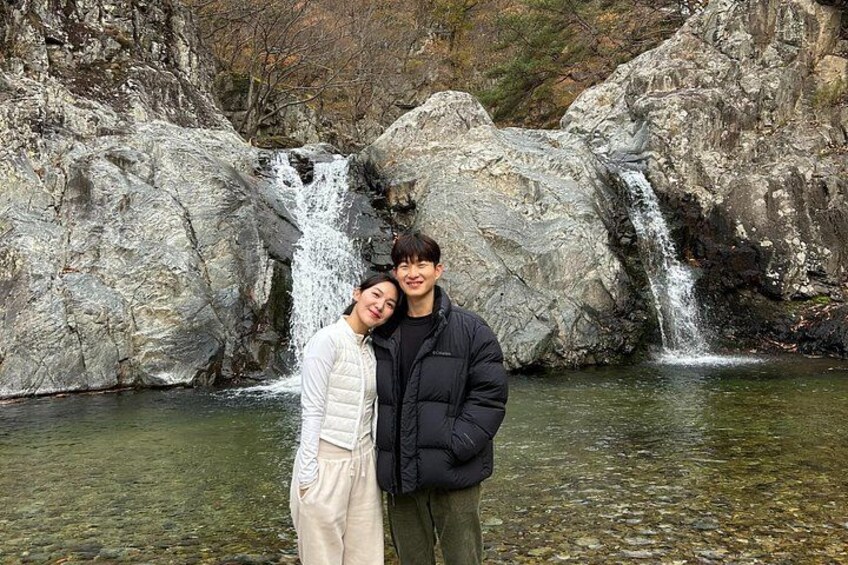 A waterfall with two people standing in front of it. 1