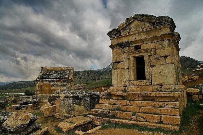 Ancient stone ruins with a central structure featuring a doorway, surrounded by scattered stones and a mountainous backdrop. 3