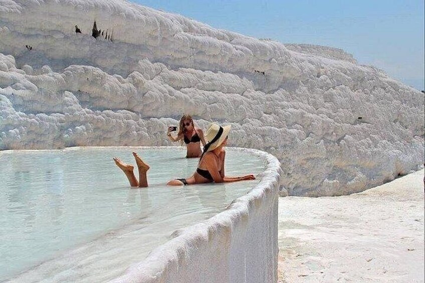 A person in a bikini sitting in a natural pool with white mineral formations in the background. 4