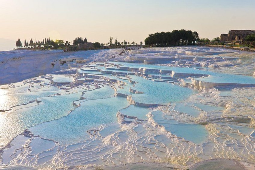 Terraced pools of clear water, a distant tree line, and a building in the background. 3