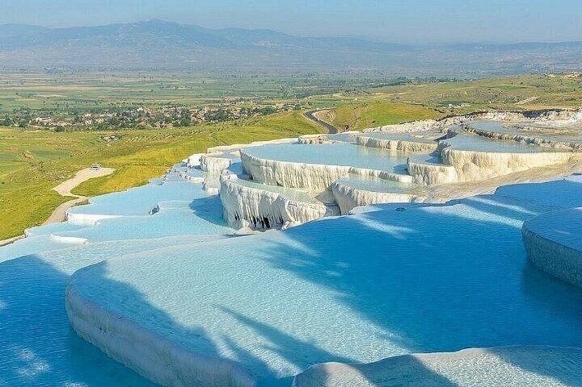 Terraced pools of clear water, a road, and distant mountains. 3