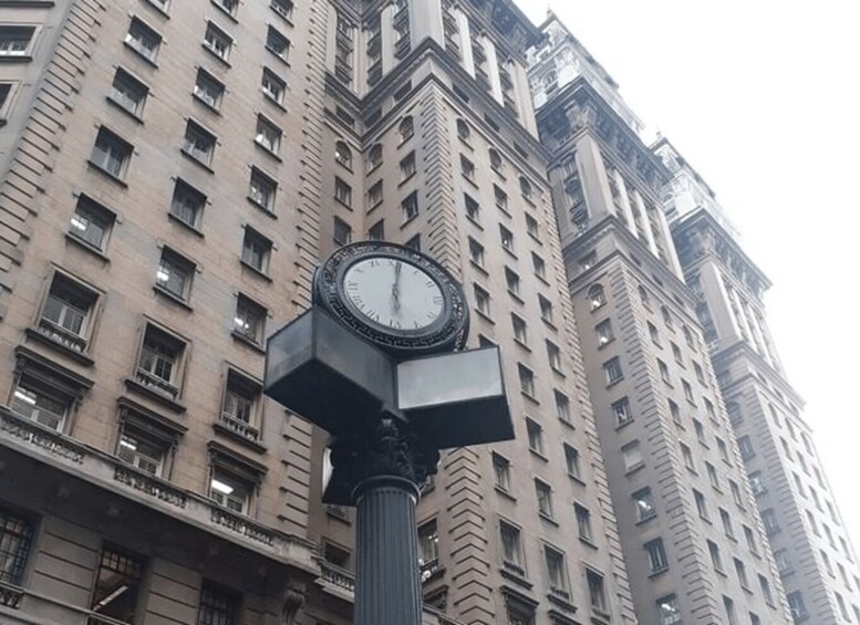 A clock on a pole in front of a tall building. 4