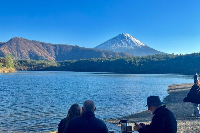 A lake with a mountain in the background, people sitting by the shore, and a clear sky. 4