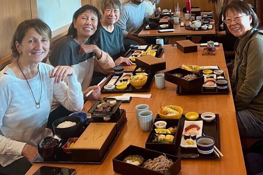 A group of people seated at a wooden table with various dishes and bowls of food. 2